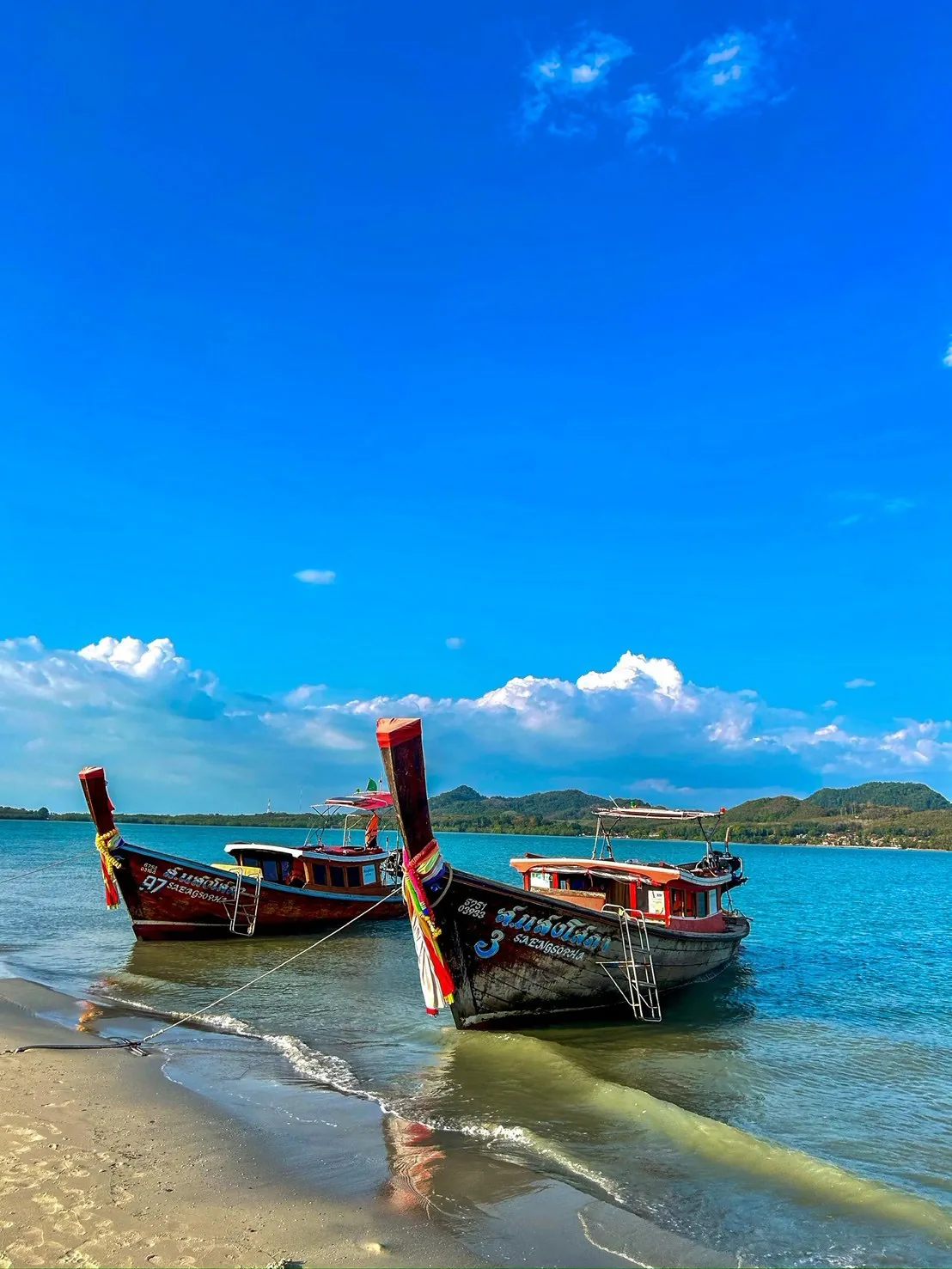 Two long-tail boats moored on an Andaman beach under a bright blue sky