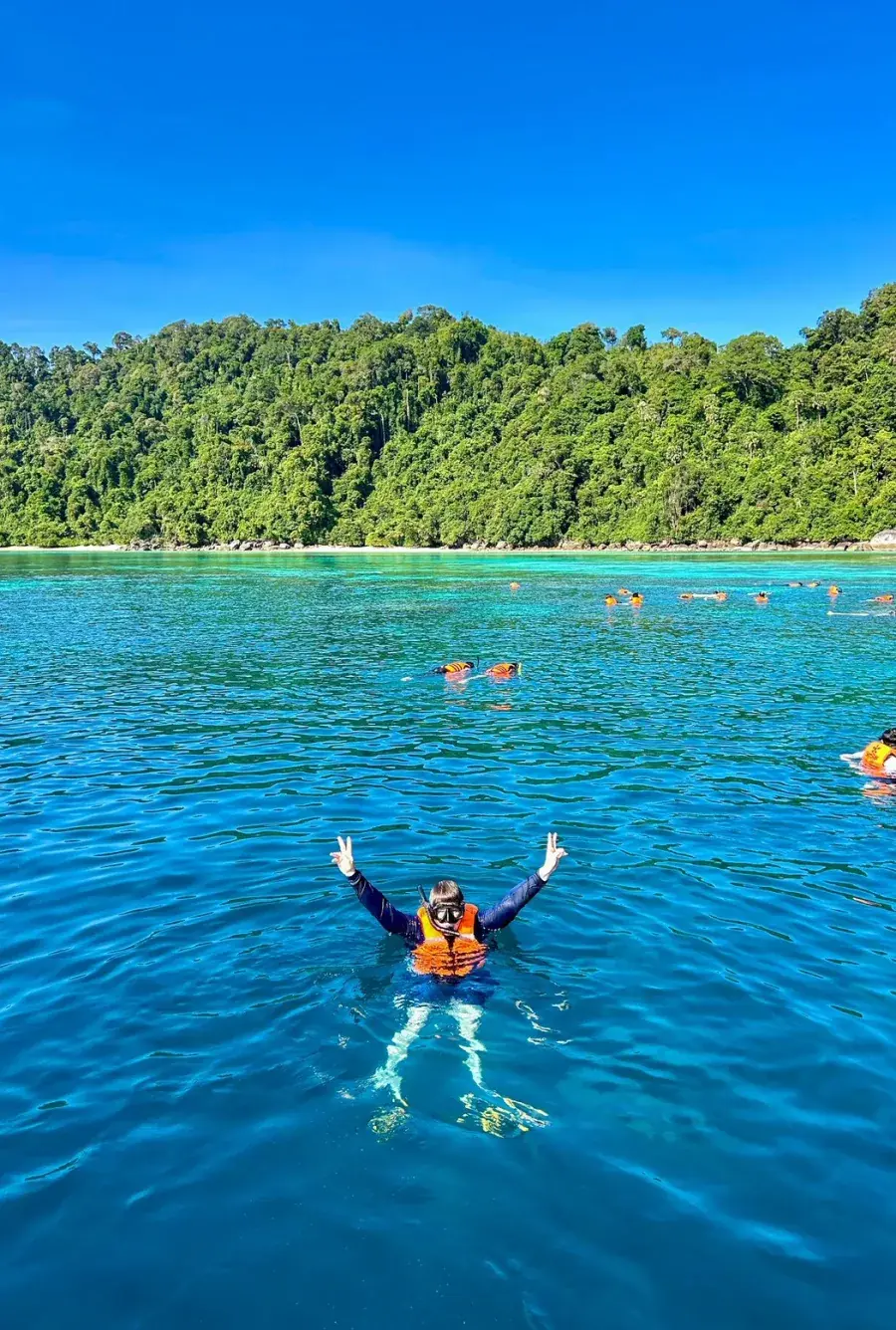 Snorkeller waving in clear deep-blue water at the Surin Islands