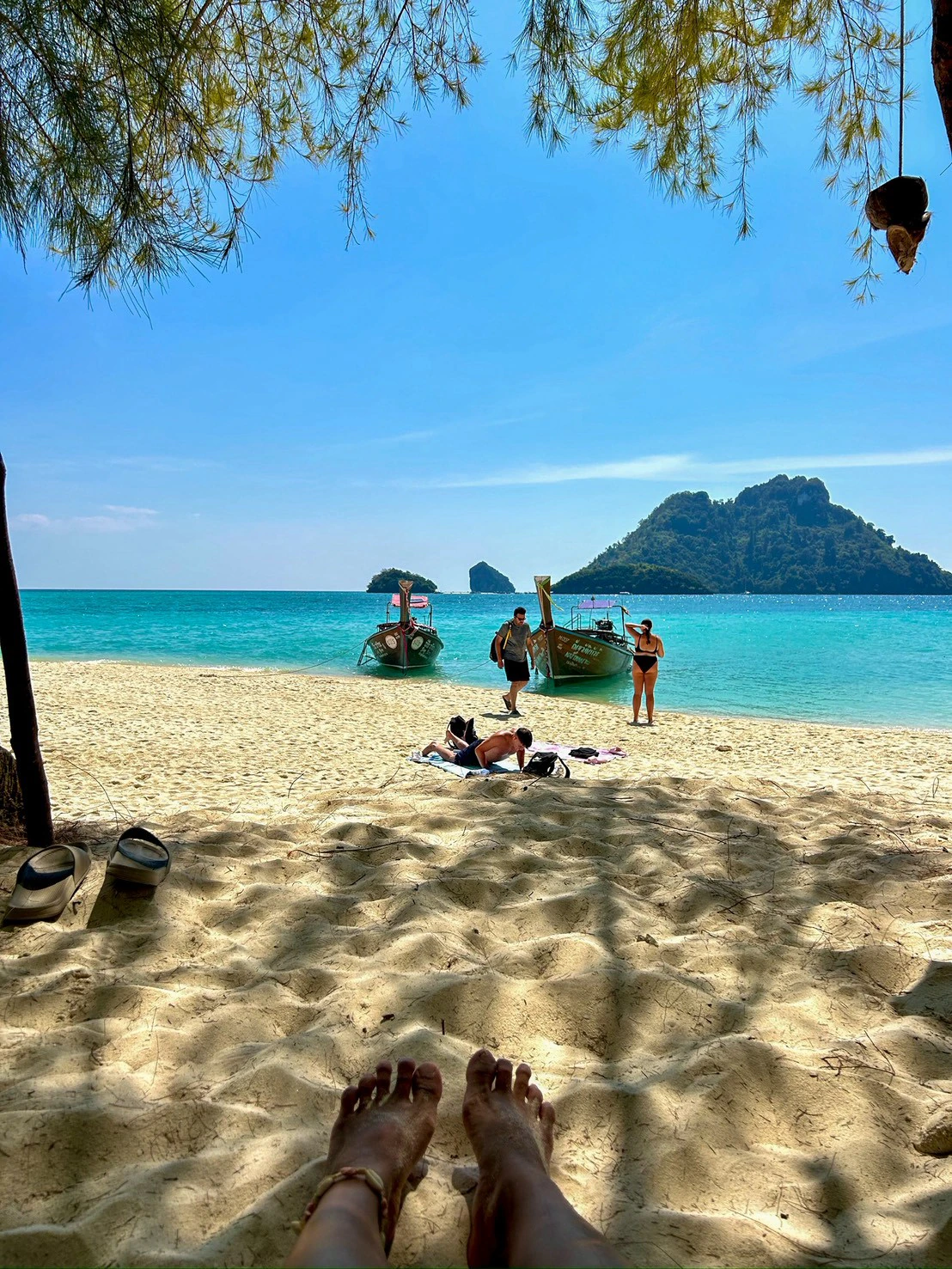หาดทรายขาวและน้ำทะเลใสสีเทอร์ควอยซ์กับเรือหางยาวและเกาะกลางทะเล